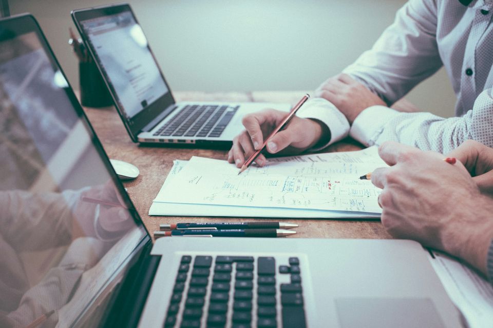 Dos personas en una mesa con portátiles dibujando a lápiz un plan de trabajo en papel